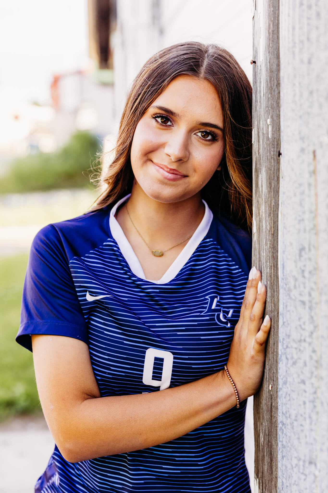 high school girl leaning against a building and smiling softly 