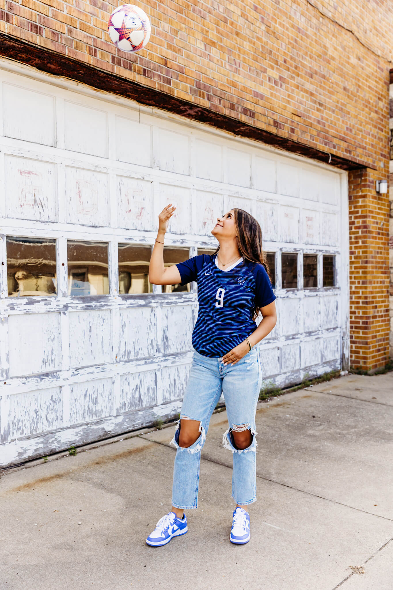 Teen girl playing with her soccer ball in front of a white garage door.