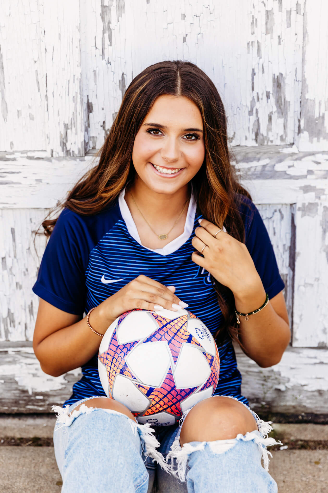 St. Norbert Soccer Camp participant sitting on the ground with a soccer ball on her lap.