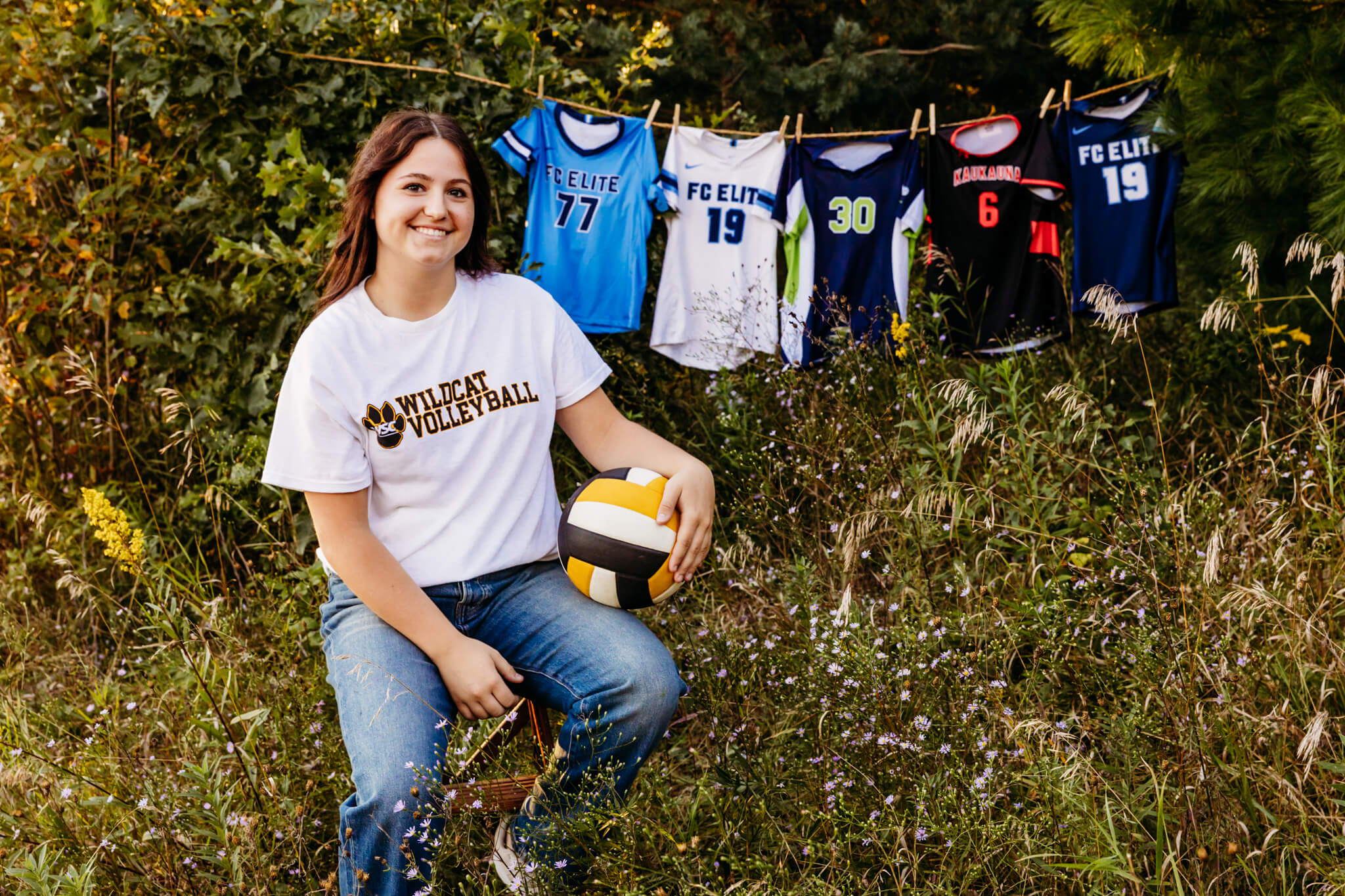 high school girl trained at UW Oshkosh Volleyball Camp, sitting in front of her volleyball jerseys while holding a ball on her lap