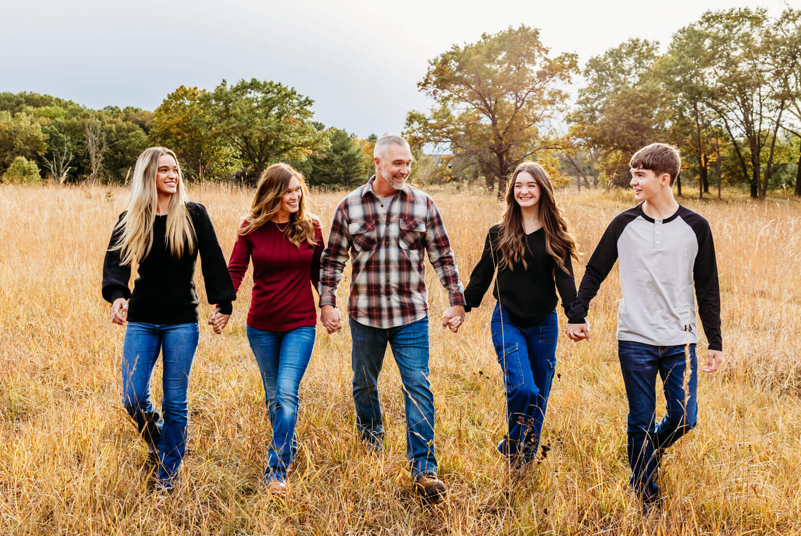 family of five with teenage children walking through a golden grass field and smiling.