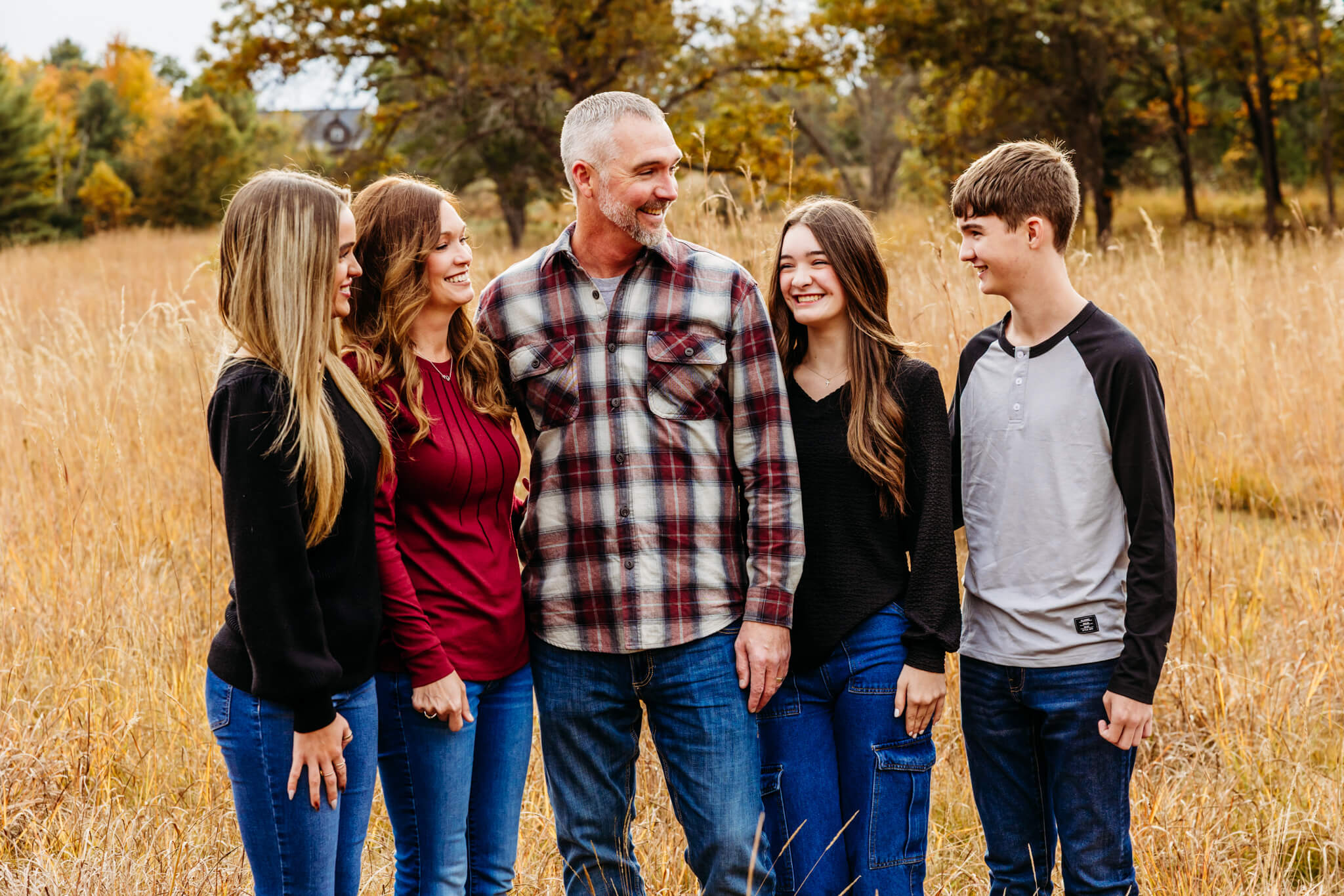 family dressed in red and black outfits laughing as they look at each other in a field near Darboy