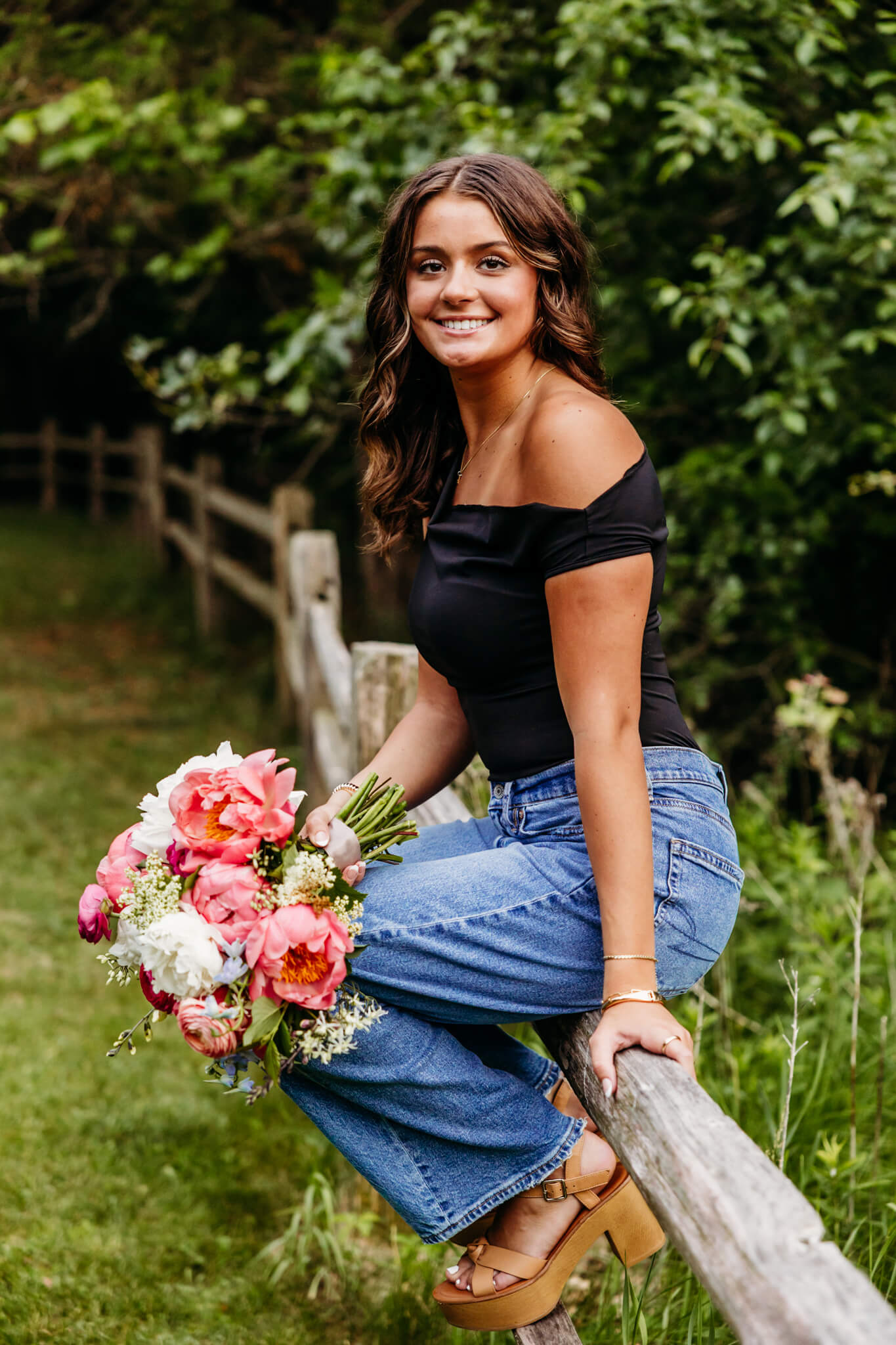 high school senior girl sitting on a fence while holding a flower bouquet