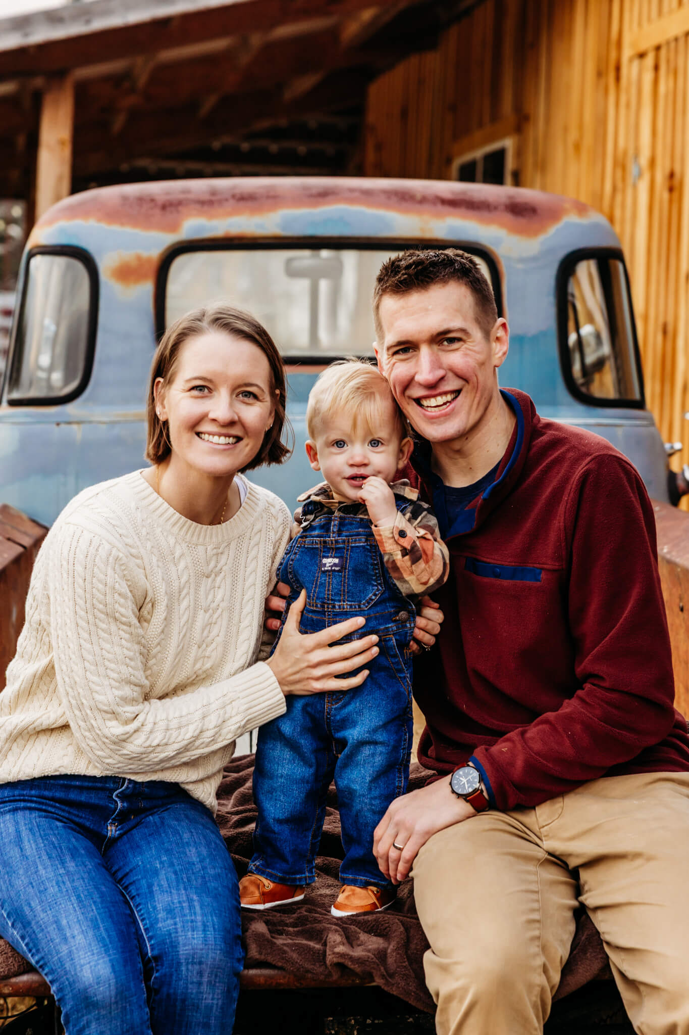 Mother and father sitting with their little boy on the back of a blue vintage truck bed at Hansen Family Choose and Cut