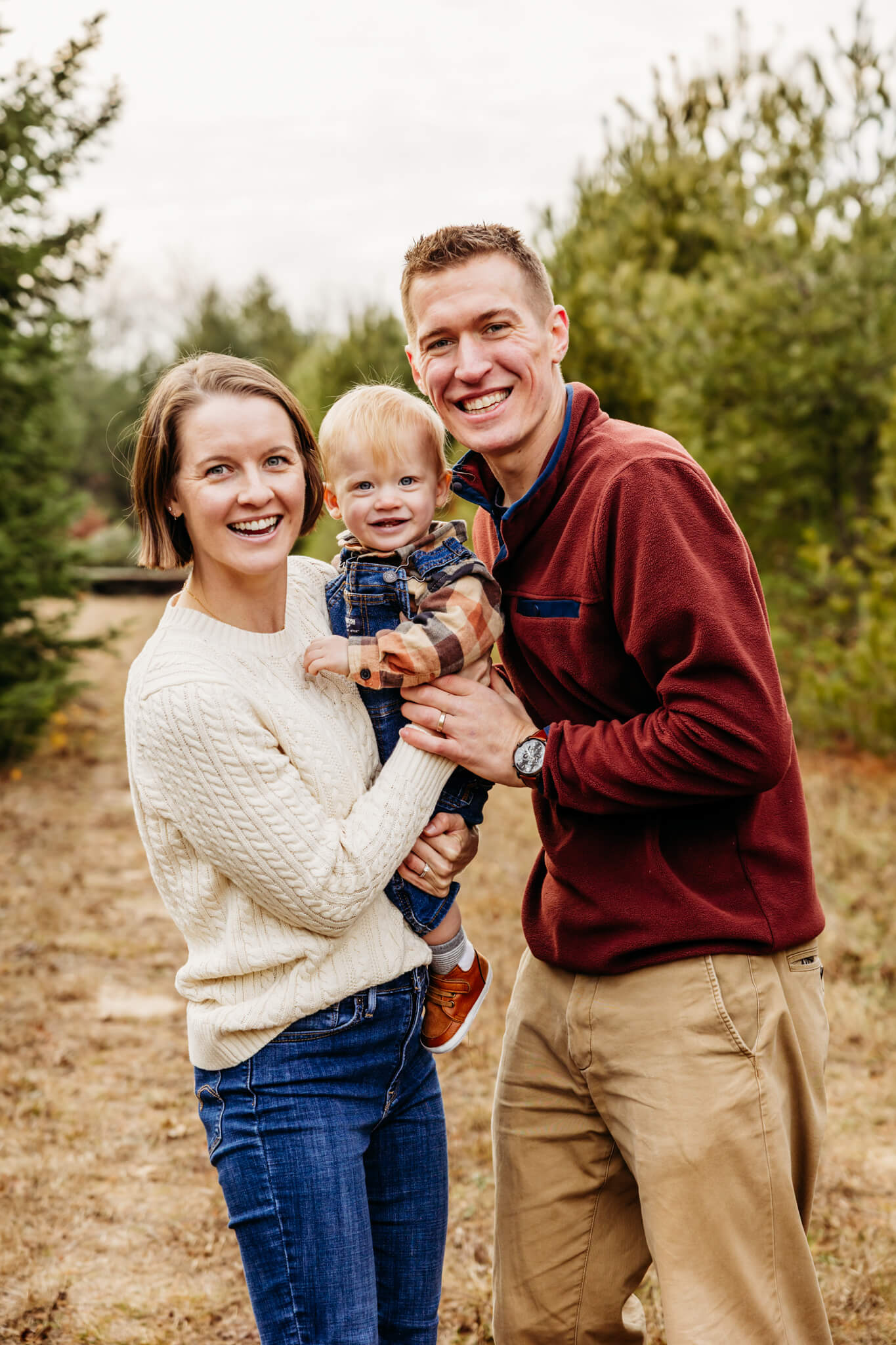 mom and dad snuggling with their little boy as they all laugh during their Christmas Tree Farm photo session.
