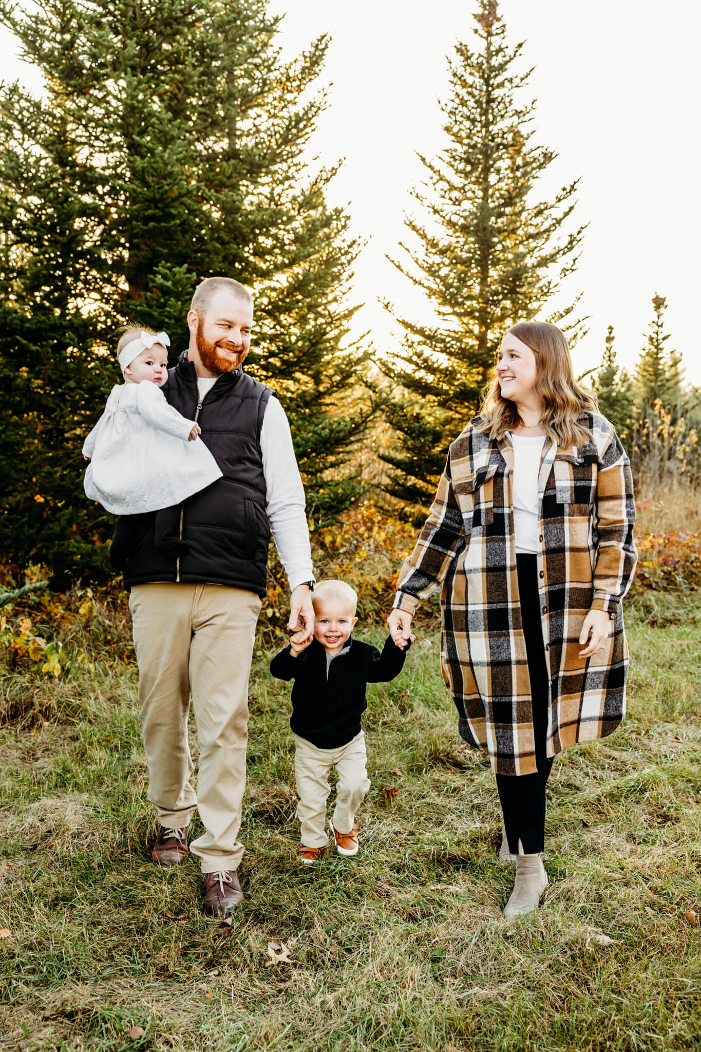 family of four in black, white and tan outfits walking at Whispering Pines Tree Farm