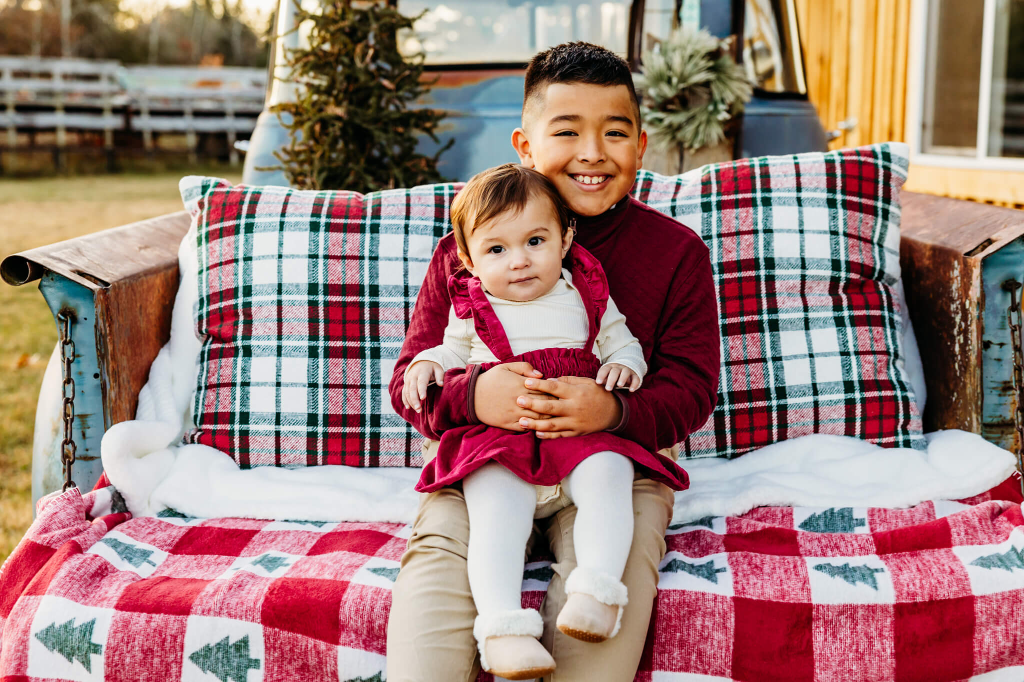 Brother holding his little sister on his lap as they sit together on a decorated vintage truck bed.