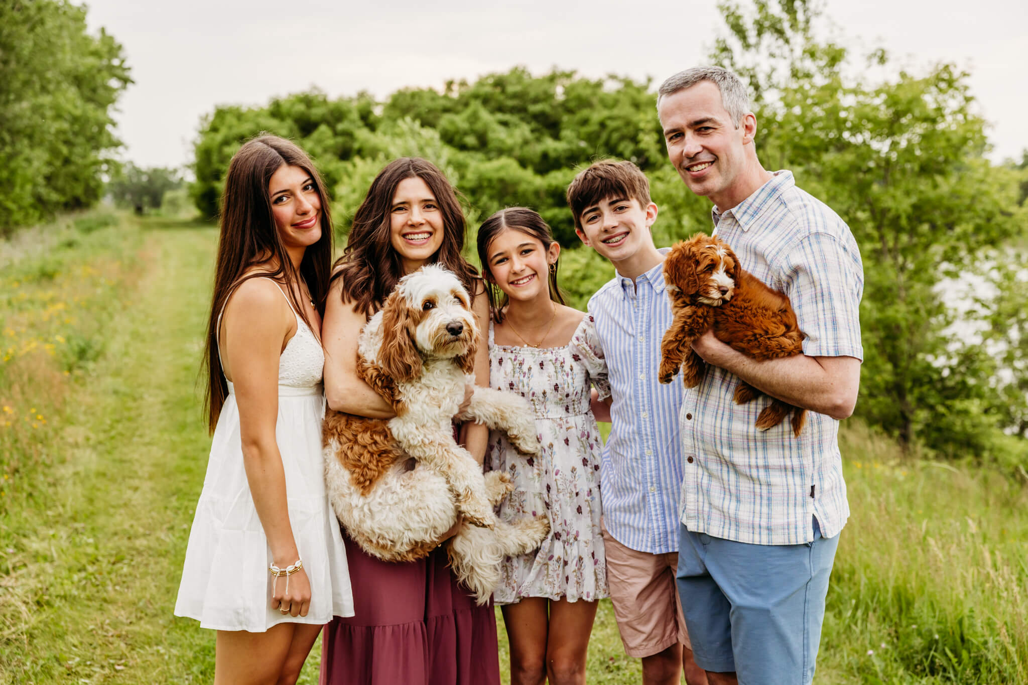 mother and father standing with their 3 teen children and two dogs while standing in a park near Appleton WI.