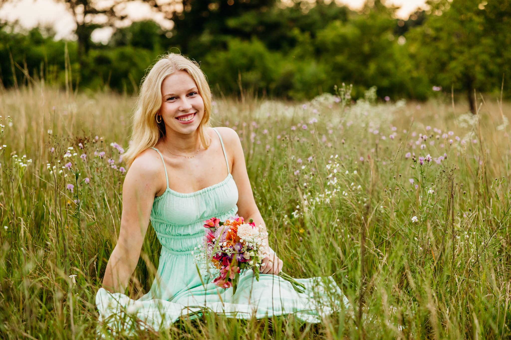 Gorgeous teenage girl in a mint colored dress holding a flower bouquet and laughing.