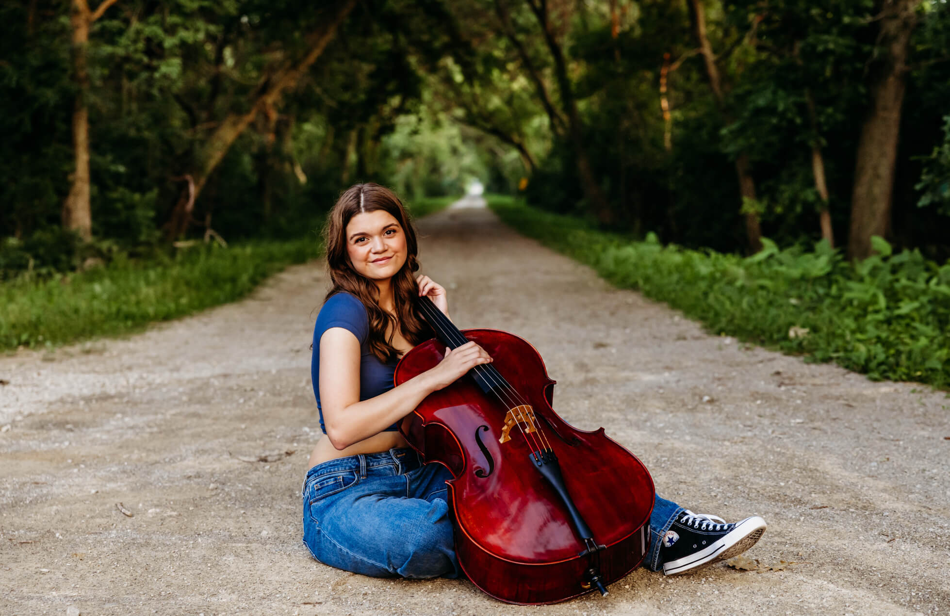 Teen girl holding a cello while sitting in the middle of Wiouwash Trail in Hortonville.