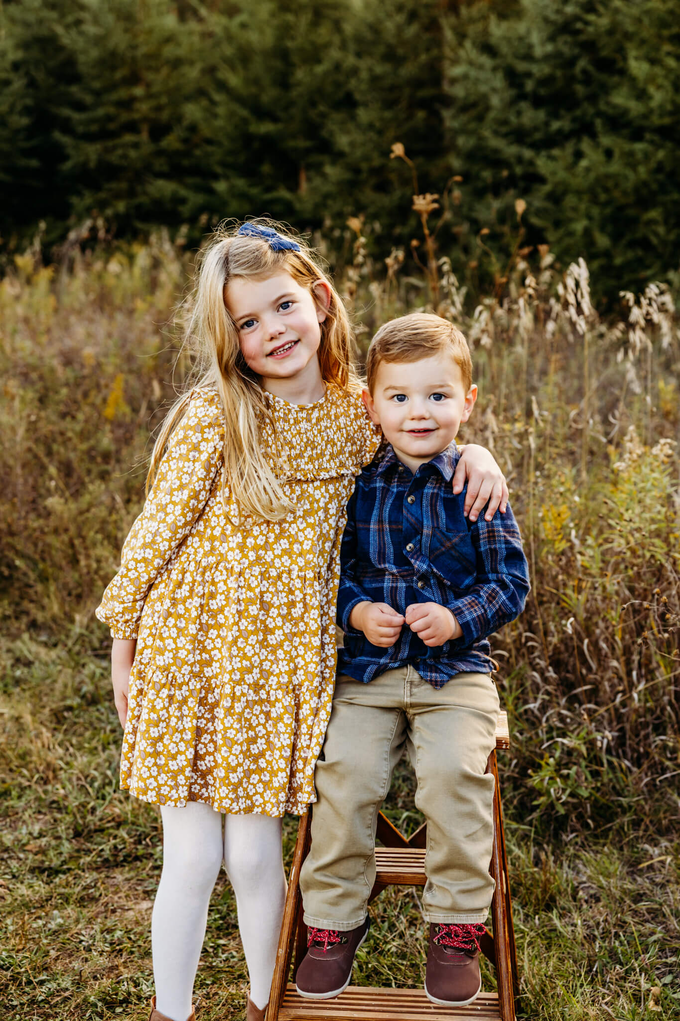 Adorable sister in a yellow dress wrapping her arm around her little brother dressed in a blue button up while walking around a pumpkin patch in Green Bay WI.