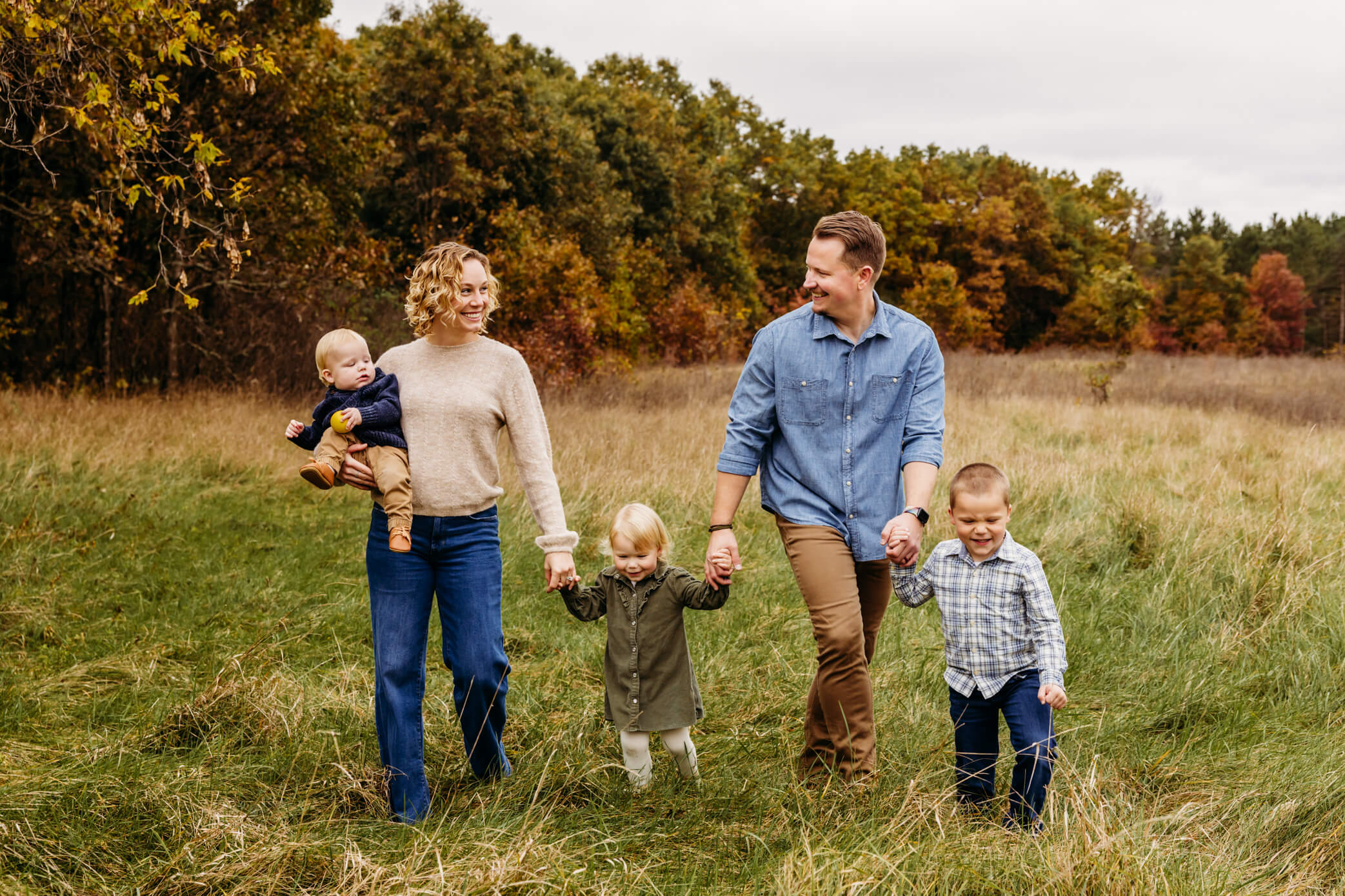Mother and father holding their children's hands as they walk together in a field.